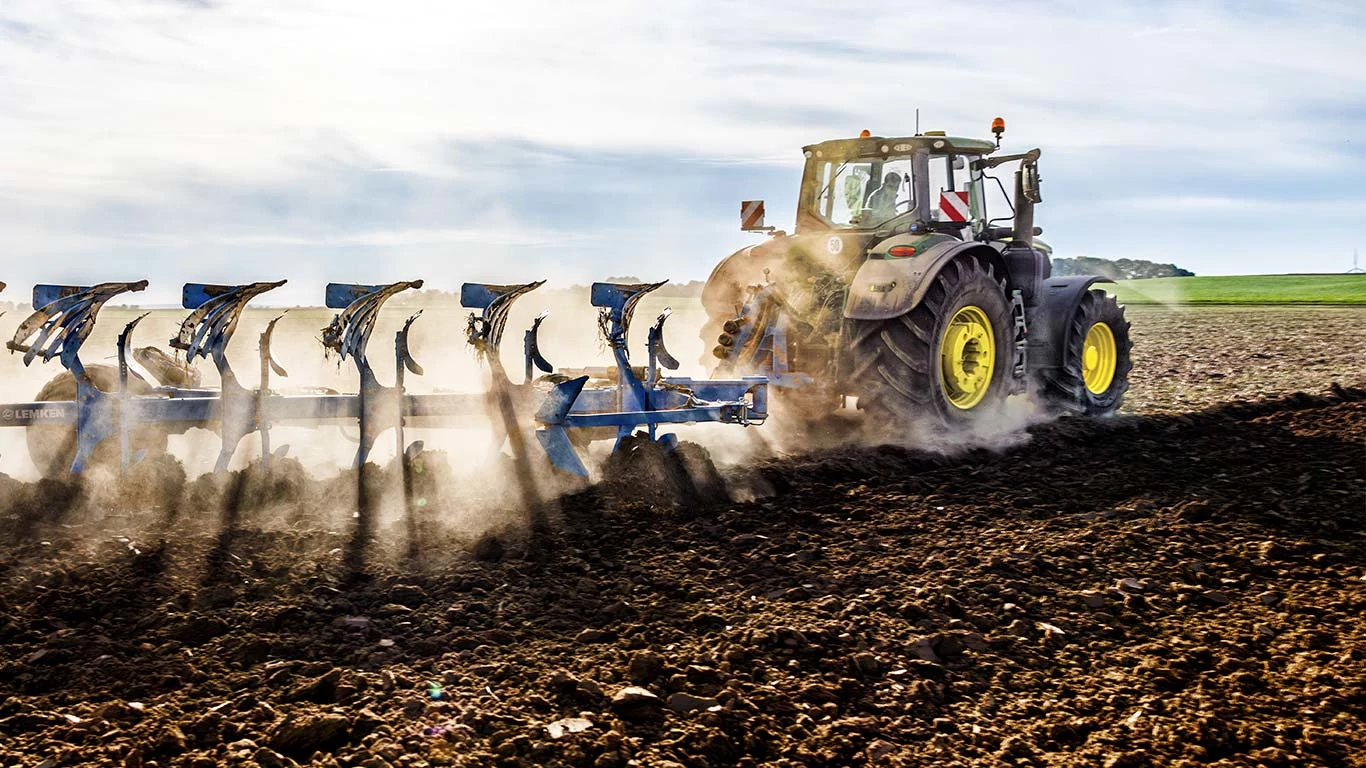 Ένα τρακτέρ που εργάζεται σε έναν αγρό, χρησιμοποιεί ένα άροτρο για την προετοιμασία της γης για μελλοντικές καλλιέργειες και την ενίσχυση της γεωργικής παραγωγικότητας.