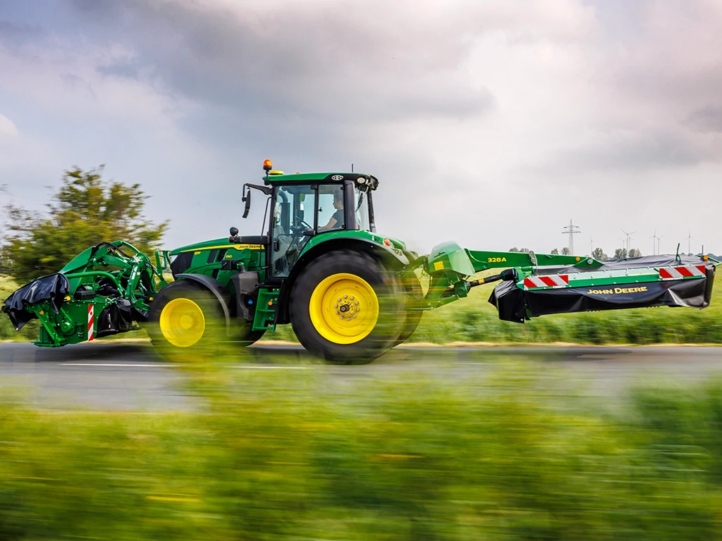 Το τρακτέρ κινείται σε δρόμο τραβώντας ένα χορτοκοπτικό-συνθλιπτικό 320A με πίσω πτερωτή