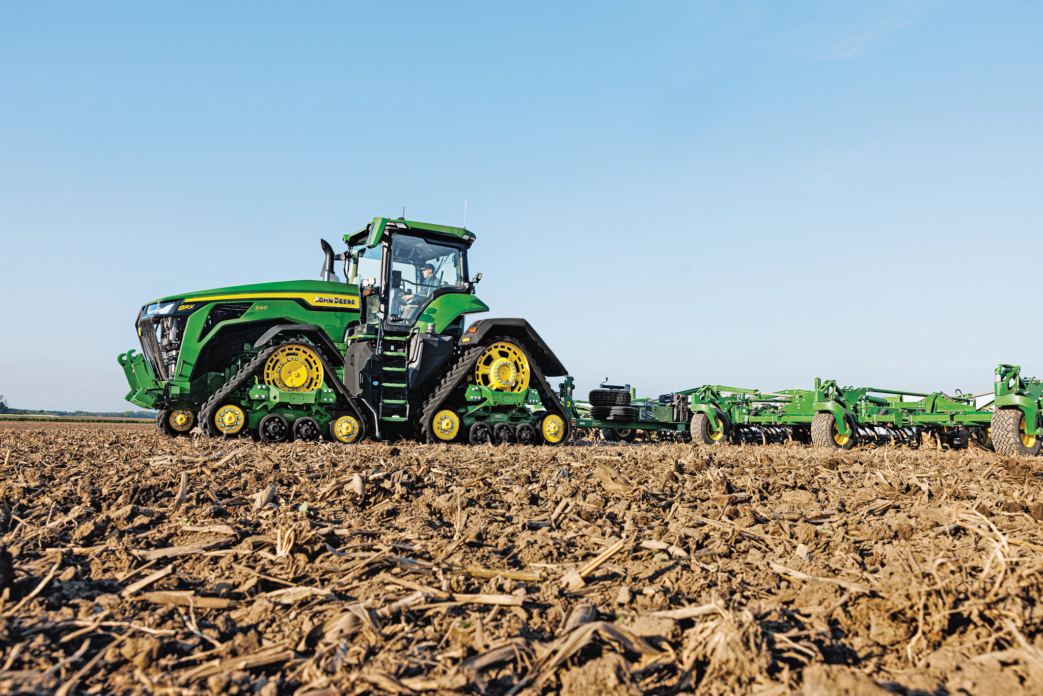 Όψη αριστερής πλευράς του τρακτέρ 8RX 540 που έλκει ένα καλλιεργητικό μηχάνημα αγρών 2230FH μέσα από έναν αγρό