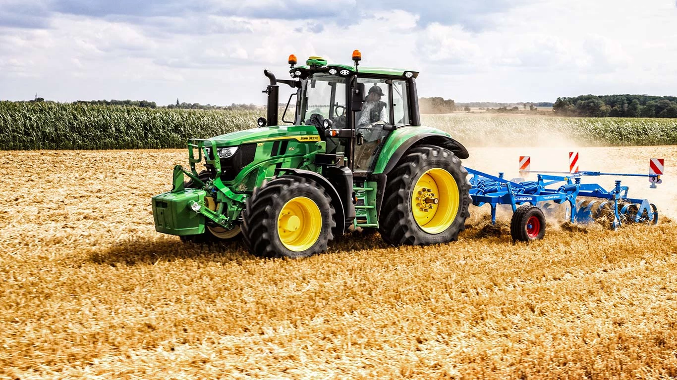 Ένα τρακτέρ οργώνει ενεργά έναν αγρό, περιστρέφοντας το έδαφος για τη φύτευση καλλιεργειών σε αγροτικό τοπίο.