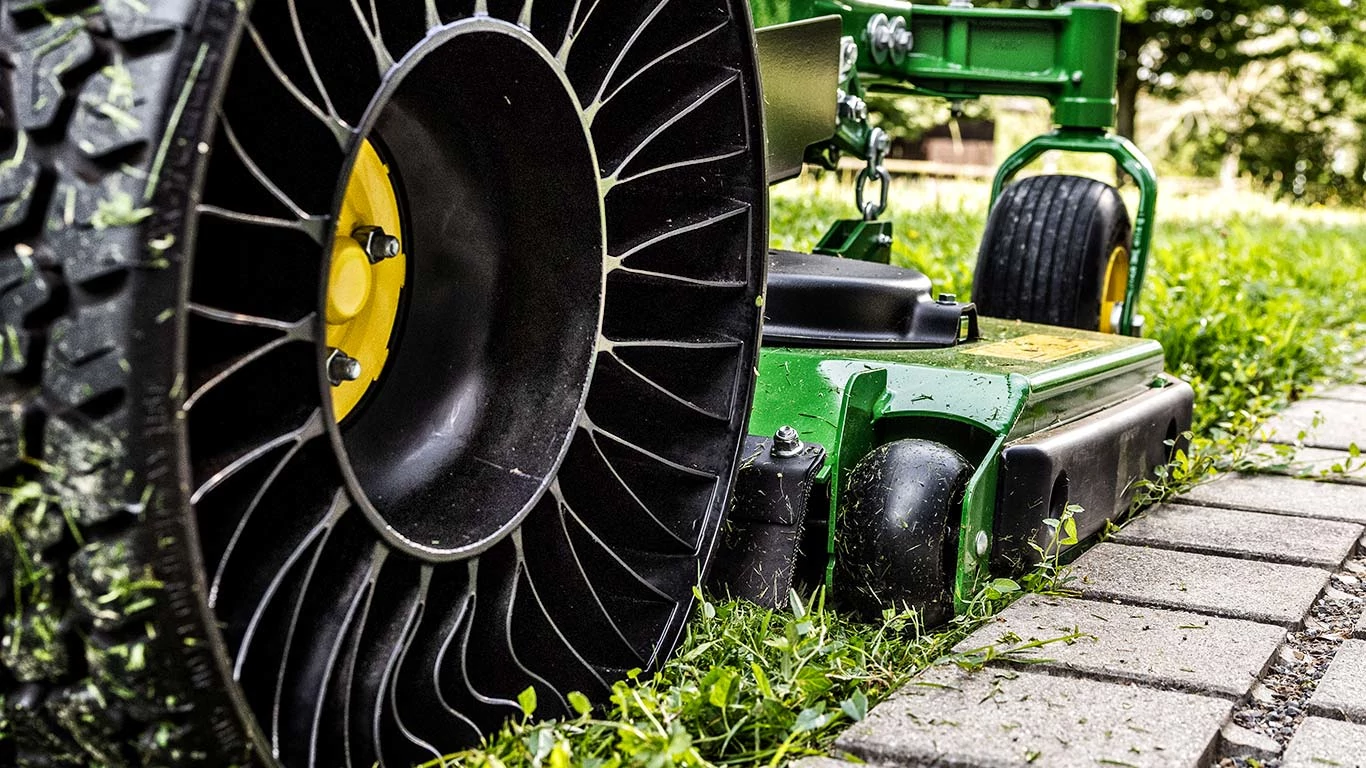 Ένα πράσινο χορτοκοπτικό με ελαστικό, τοποθετημένο σε καλά συντηρημένο γκαζόν, επιδεικνύοντας το ζωντανό χρώμα και τον σχεδιασμό του.