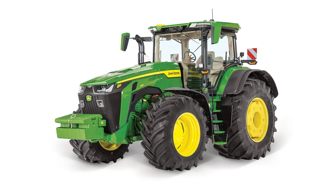 Απεικονίζεται το τρακτέρ 8R της John Deere με γωνία εμπρός-δεξιά σε λευκό φόντο, με μεγάλα πίσω ελαστικά, μπροστινό μπλοκ αντίβαρων και πλήρη καμπίνα