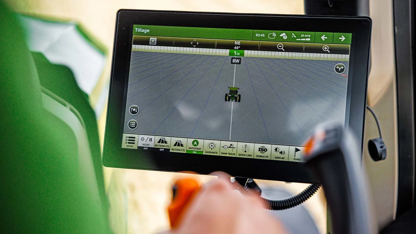 Ένα άτομο εξετάζει ένα tablet που εμφανίζει πληροφορίες από την οθόνη ενός τρακτέρ, οι οποίες δείχνουν τη σύγχρονη γεωργική τεχνολογία.