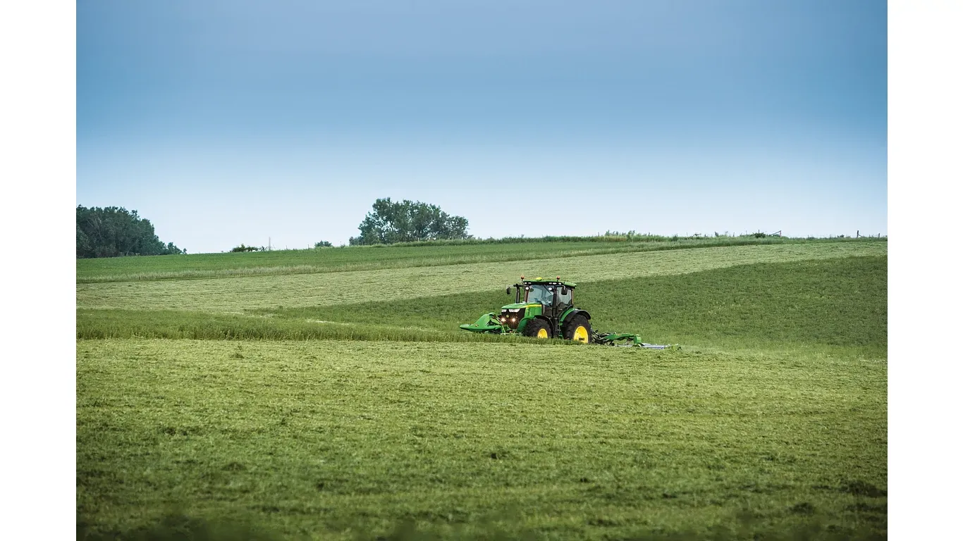 Απεικονίζεται το πίσω χορτοκοπτικό R350R της John Deere που κόβει χόρτο σε μεγάλο χωράφι, με το τρακτέρ να εργάζεται σε έδαφος με απαλές κλίσεις.