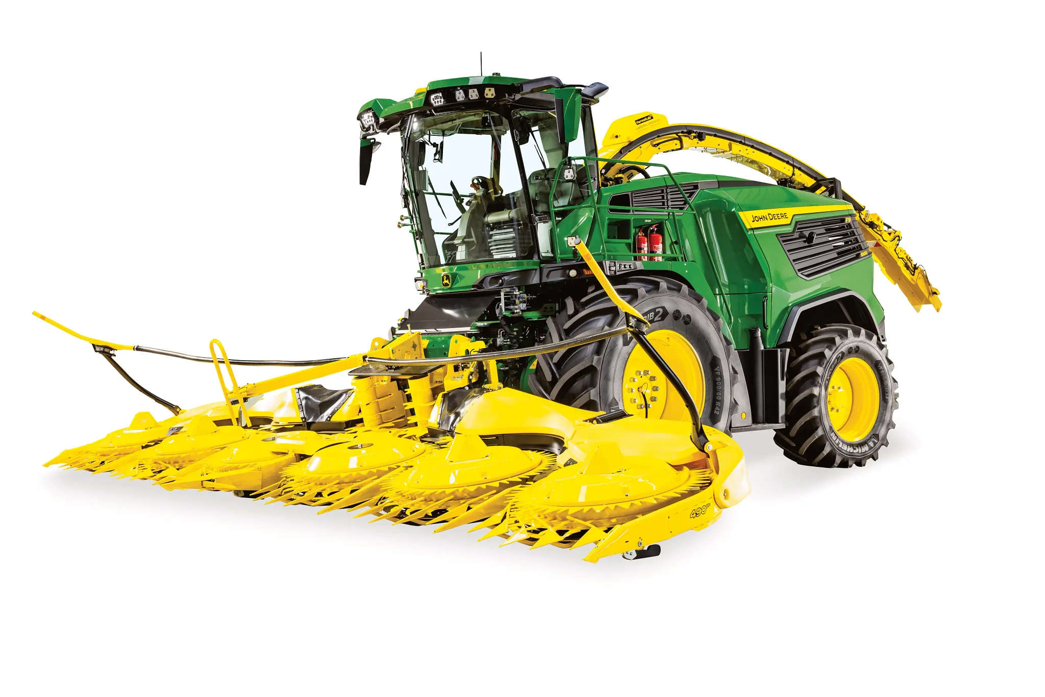 Το ενσιρωκοπτικό μηχάνημα John Deere με μεγάλη κεφαλή καλαμποκιού και ανυψωμένο καμπυλωτό στόμιο σωλήνα εκκένωσης απεικονίζεται από την γωνιακή μπροστινή πλευρά σε λευκό φόντο.