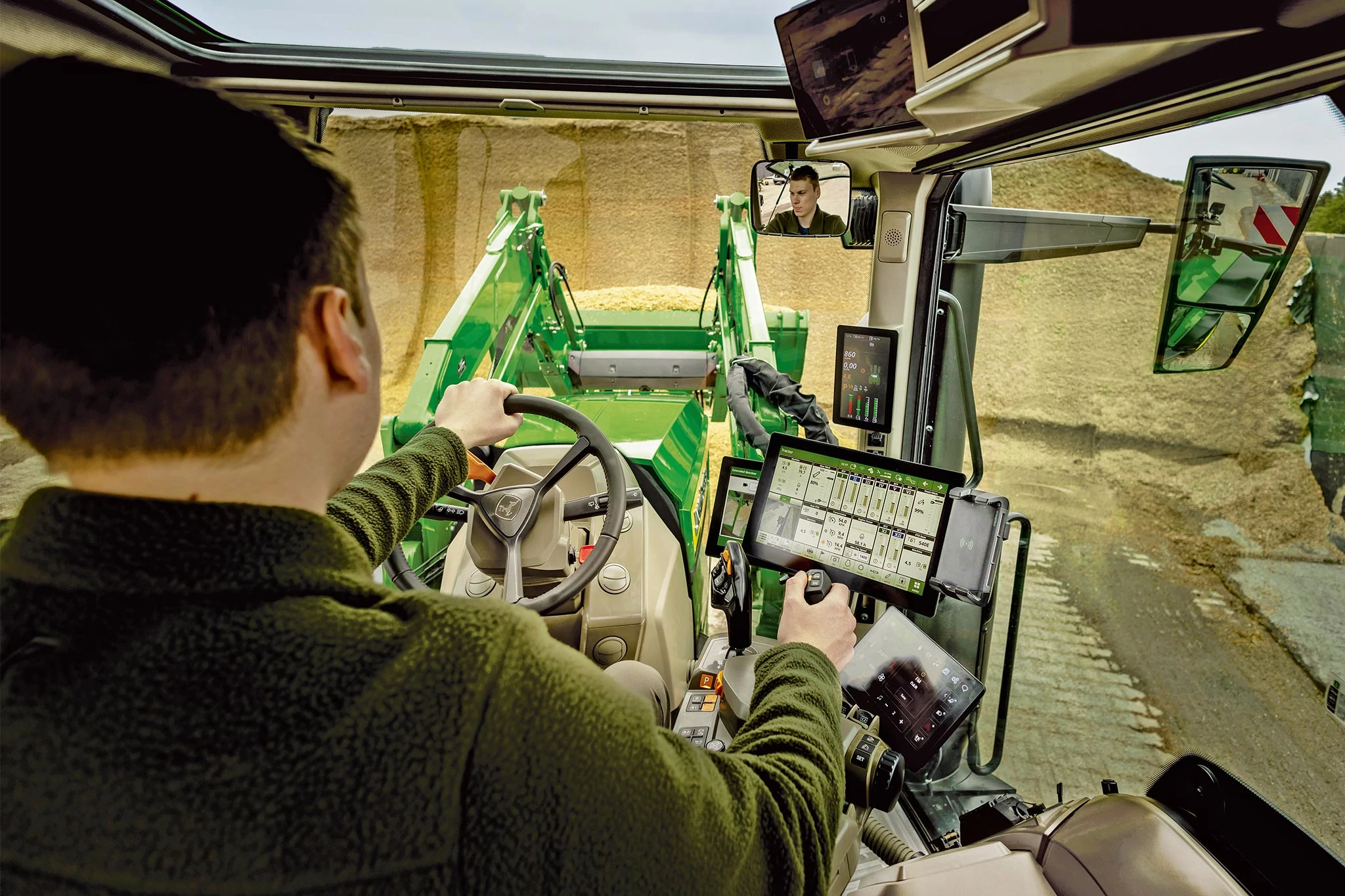 Interior cab view of John Deere tractor showing operator controls and front loader operation.