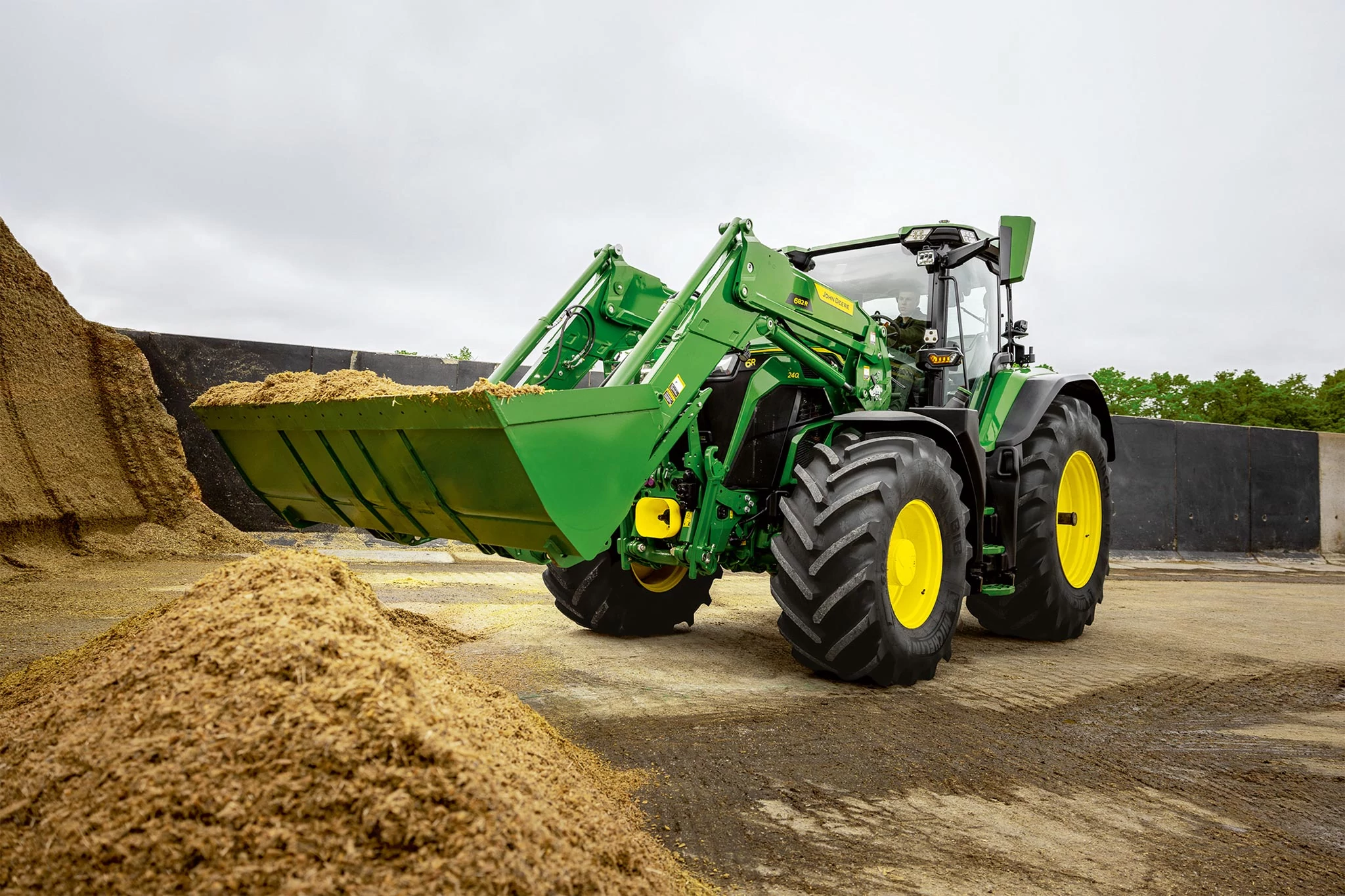Front loader bucket filled with silage on a John Deere tractor during material handling work.
