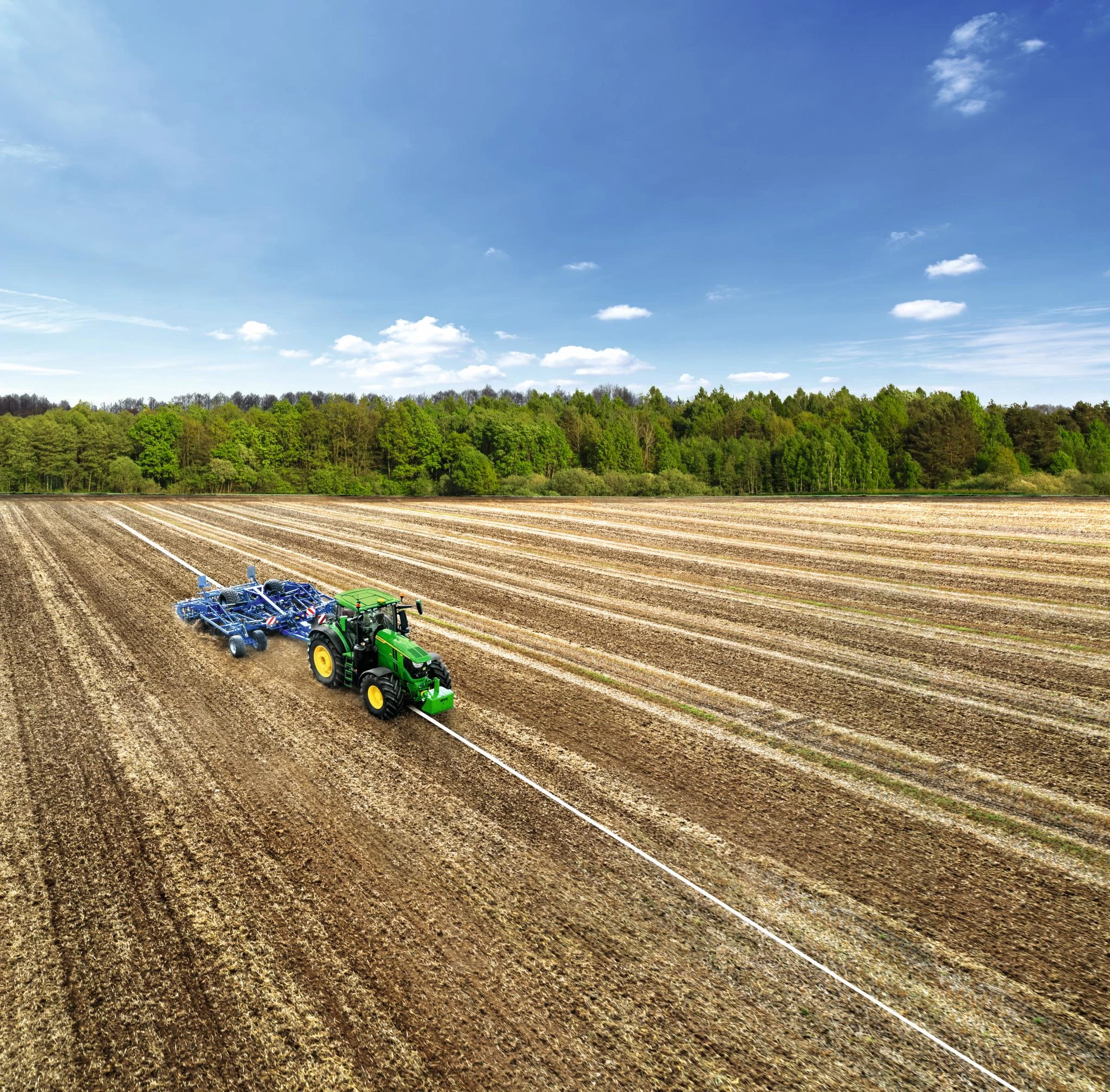 Precision farming tractor cultivating a large field in straight rows, aerial view showing soil preparation and efficient field coverage.