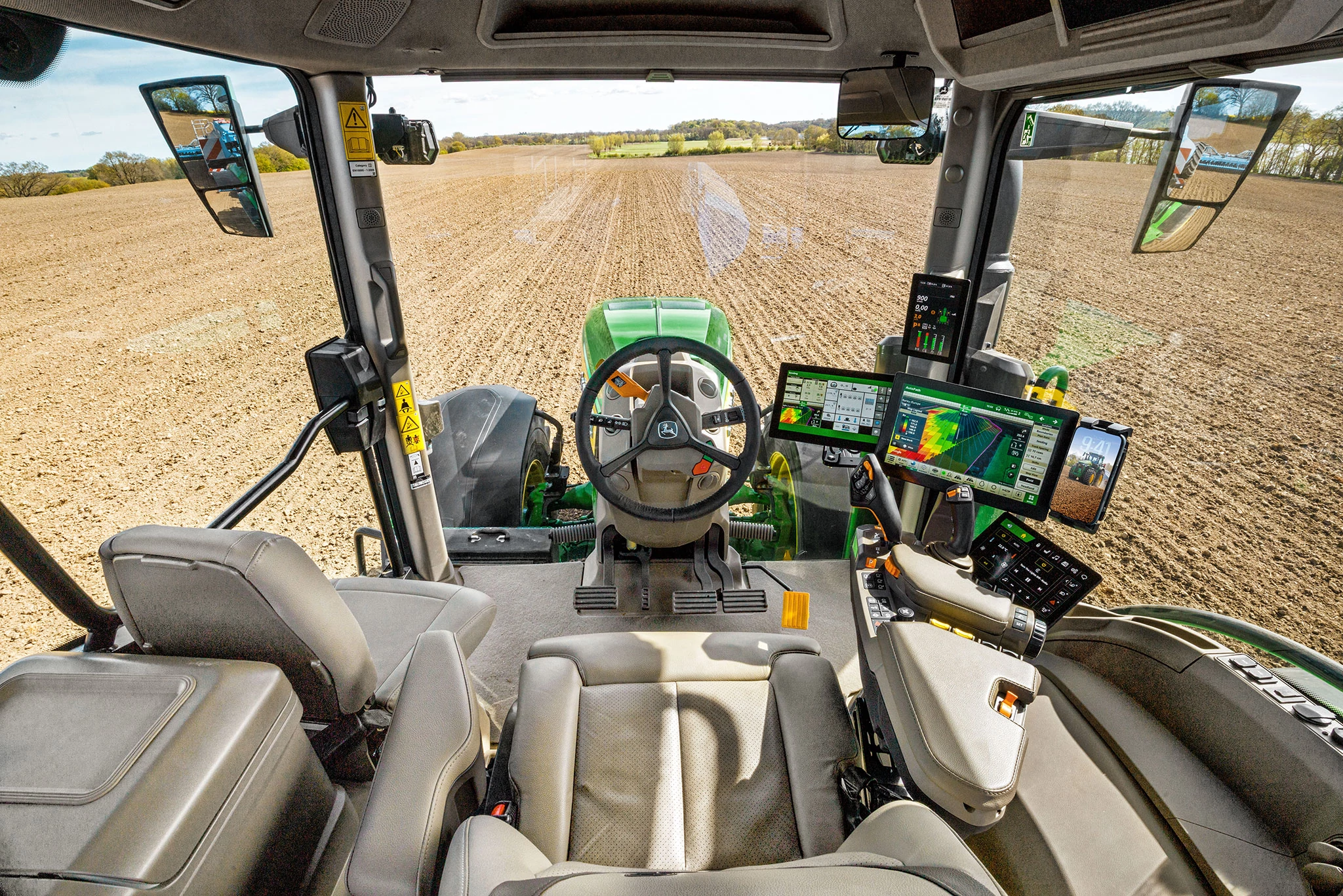 John Deere 8R cab view with steering wheel and precision farming displays overlooking prepared field