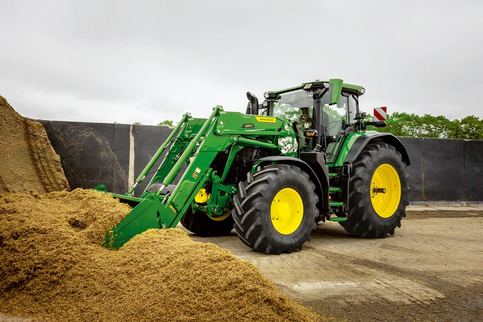 John Deere tractor pushing into a silage pile with front loader bucket in farm environment.